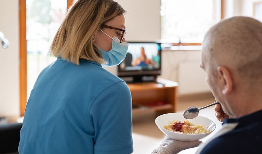 Woman in blue feeding a senior