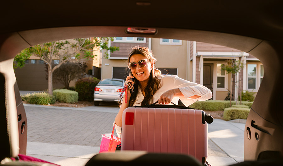 Woman putting a pink suitcase in the trunk of her car